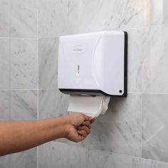 a hand holding a roll of toilet paper in front of a wall mounted urinal