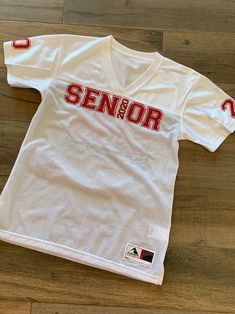 a white jersey with the word senior on it sitting on top of a wooden floor