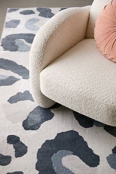 a white chair sitting on top of a rug next to a pink and blue pillow