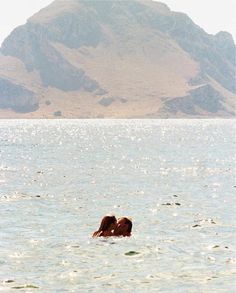 two people are swimming in the ocean with mountains in the background and one person is kissing the other