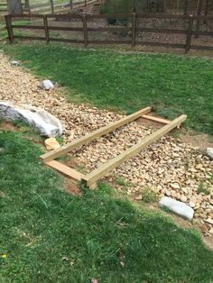 a wooden frame laying on top of rocks in the grass next to a rock and wood fence