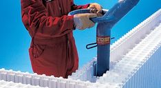 a man in a red suit is working on a white fence with a blue pipe