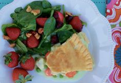 a white plate topped with a pie next to a pile of strawberries and spinach