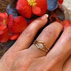 a woman's hand with a ring on it and red flowers in the background