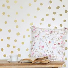 a table with a book, cup and saucer on it next to a polka dot wallpaper