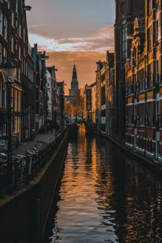 the sun is setting on an old city street with water running through it and buildings along both sides