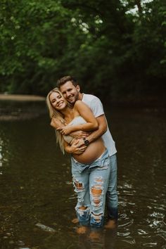 a man and woman hugging in the middle of a river with trees in the background