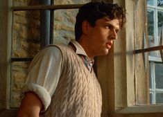 a man in a sweater vest standing next to a window