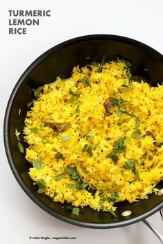 a pan filled with yellow rice on top of a black table next to utensils