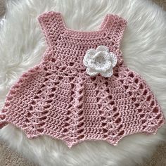 a pink crocheted dress with a white flower on the front and side, sitting on a fur rug