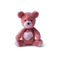 a pink crocheted teddy bear with a heart on it's chest sitting in front of a white background