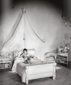 black and white photograph of a woman laying in bed with her dog on the floor