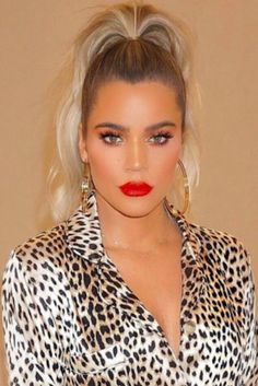 a woman with blonde hair wearing a leopard print shirt and red lipstick is standing in front of a beige wall