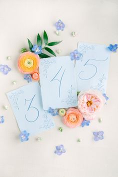 the table numbers are displayed on blue paper with flowers and leaves around them, as well as pink roses