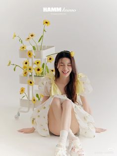 a woman sitting on the ground with sunflowers in front of her and a vase behind her