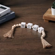 the word home spelled with wooden beads and tassels next to a potted plant