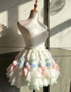 a white mannequin with pink and blue crocheted skirt on display in front of a wall