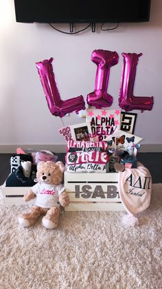 a teddy bear sitting on top of a box filled with pink balloons and other items