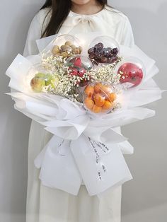 a woman holding a bouquet of fruit and flowers