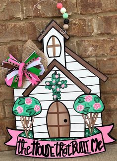 a paper cut out of a house with flowers and trees on it, hanging from the side of a brick wall