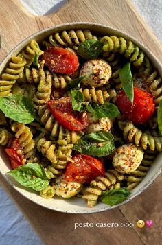 a bowl filled with pasta and vegetables on top of a wooden cutting board