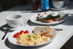 two plates with eggs, bread and tomatoes on them sitting on a table next to coffee cups