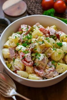 a white bowl filled with potato salad next to some tomatoes and other vegetables on a wooden table