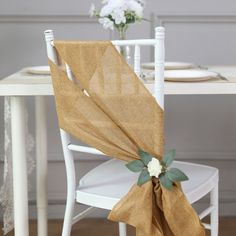 a table with white chairs and a brown cloth draped over the back of it's chair