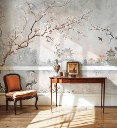 a room with a desk, chair and wallpaper on the walls that has birds painted on it