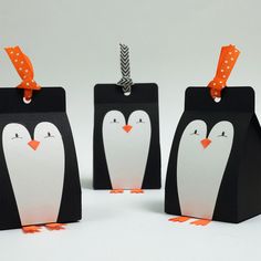 three penguin shaped gift bags with tags attached to them, one is black and the other is white