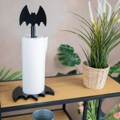 a toilet paper holder with a bat cut out on it next to a potted plant