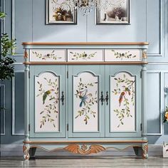 a blue cabinet with flowers and birds painted on the doors is next to a potted plant