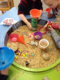 two children playing in a sand and water play area with plastic cups, spoons and food