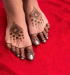 a woman's feet with hendix and jewels on their toes, sitting on a red blanket