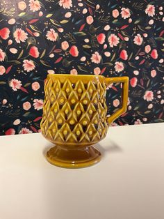 a yellow vase sitting on top of a white table next to a floral wallpaper