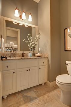 a white toilet sitting in a bathroom next to a sink under a mirror and lights