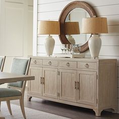 a dining room table with two lamps and a mirror on it's sideboard