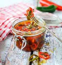 a spoon full of pickled peppers on top of a wooden table with red and white checkered cloth