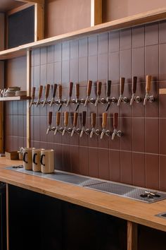 a row of beer taps mounted to the side of a brown tiled wall next to a sink