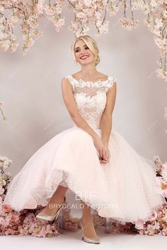 a woman in a pink dress sitting on a chair with flowers around her and smiling at the camera