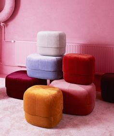 four different colored stools in front of a pink wall