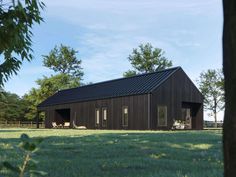 a black barn sits in the middle of a grassy field with trees and grass around it