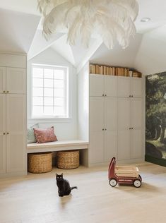 a cat sitting on the floor next to a toy car in a room with white walls