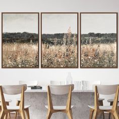 three paintings hanging on the wall above a dining room table with chairs and a vase