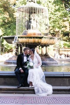 a bride and groom sitting on a bench in front of a fountain