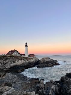 a light house sitting on top of a rocky cliff next to the ocean at sunset