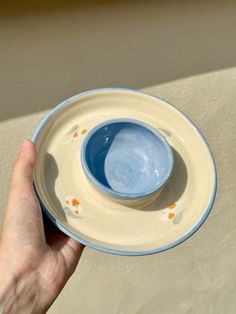 a hand holding a blue and white plate with an orange dot design on the rim