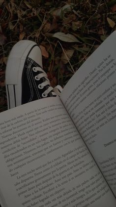 an open book sitting on the ground next to a person's feet and sneakers