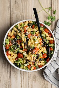 a white bowl filled with pasta salad on top of a wooden table next to a fork