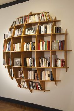 a bookshelf filled with lots of books on top of a wooden floor next to a white wall